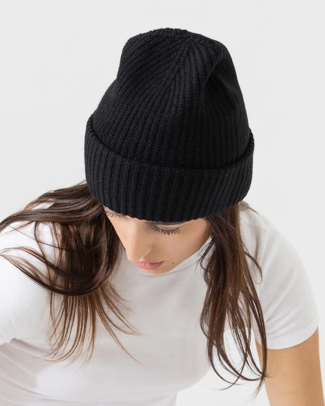 Person wearing black merino wool beanie with a white outfit on a plain background