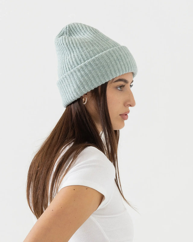 Person wearing light green merino wool beanie with a white outfit on a plain background