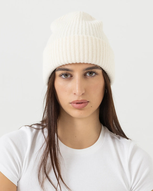 Woman wearing a white knit beanie and white t-shirt against a light gray background