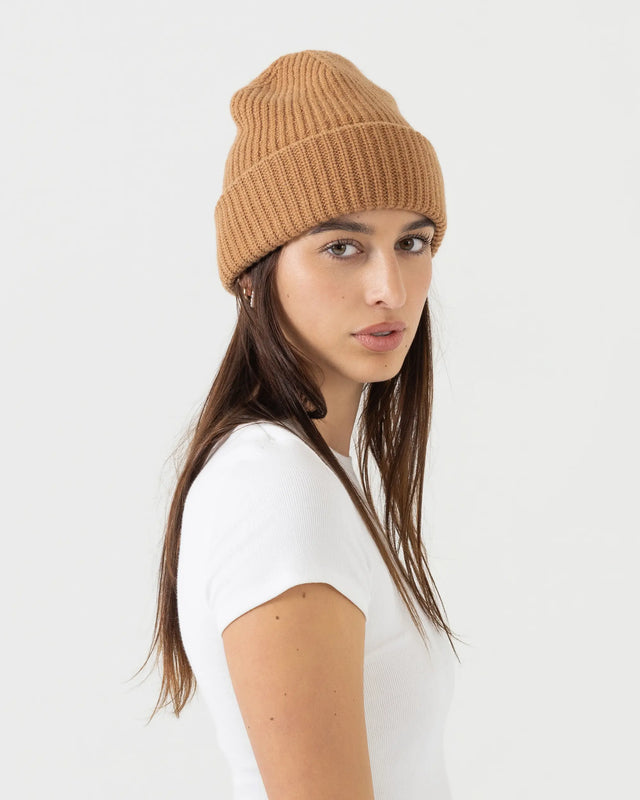 Person wearing brown merino wool beanie with a white outfit on a plain background