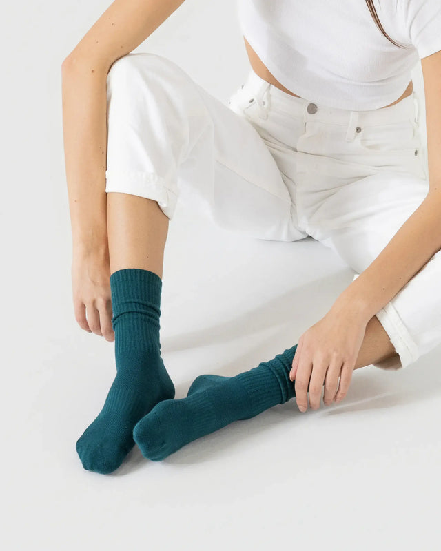 Person wearing dark green sporty socks with a white outfit on a plain background