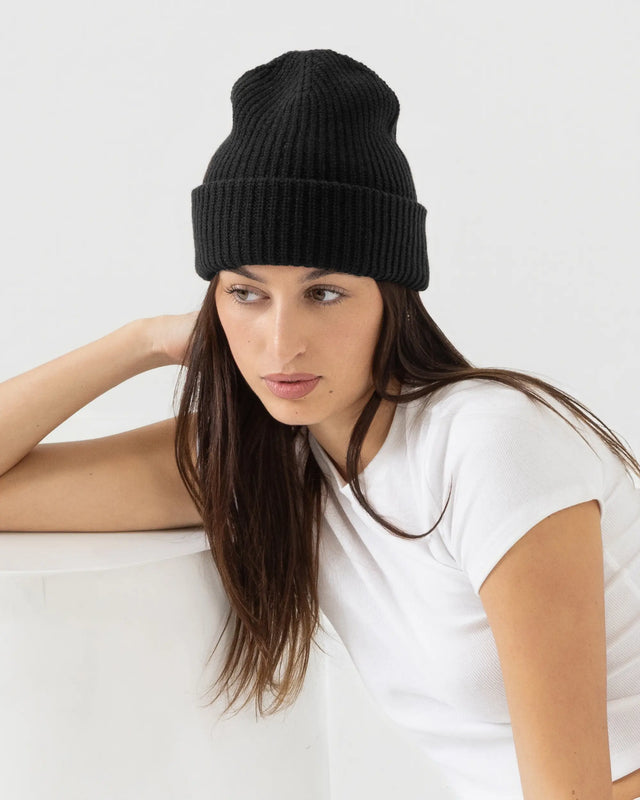 Person wearing black merino wool beanie with a white outfit on a plain background