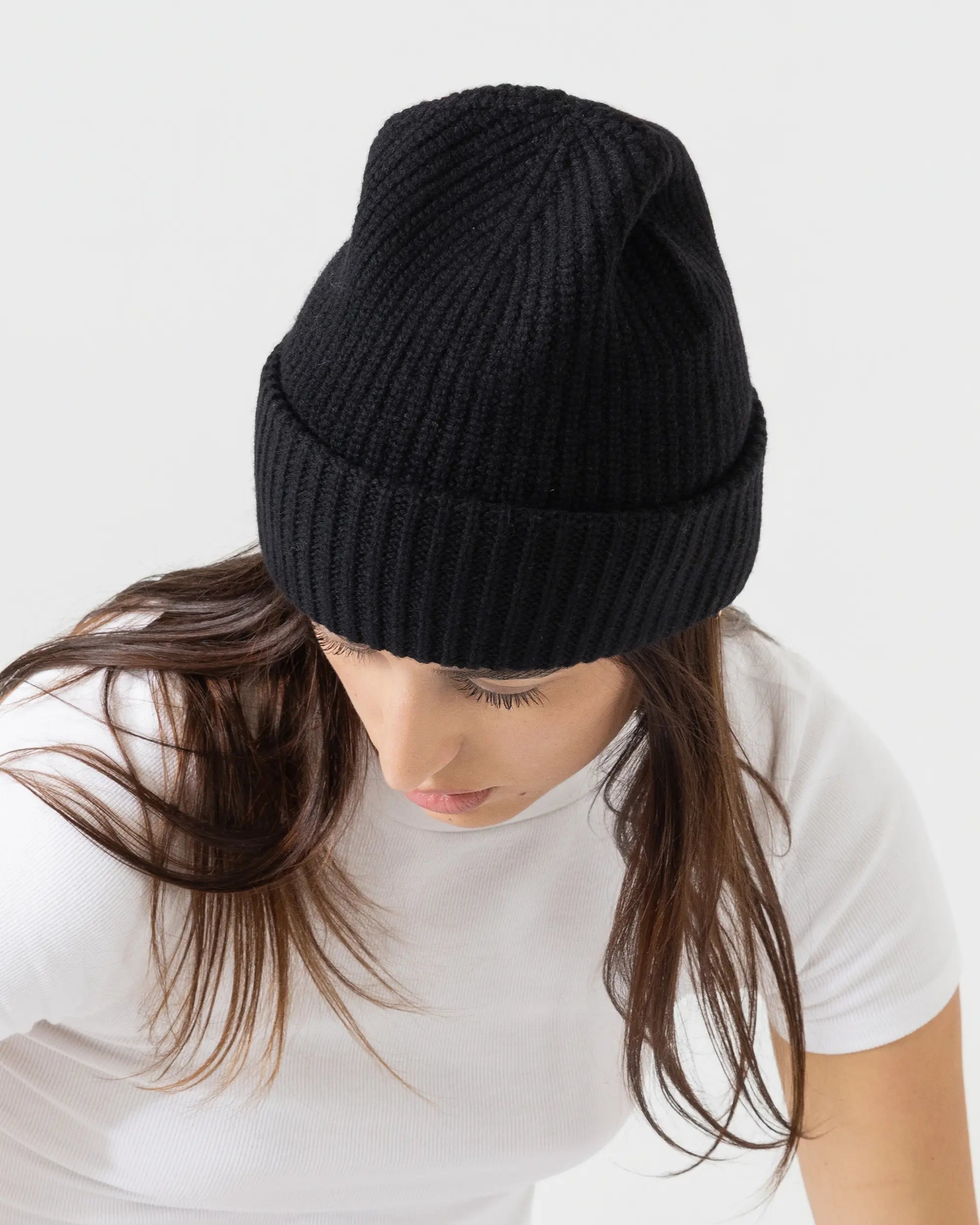Person wearing black merino wool beanie with a white outfit on a plain background