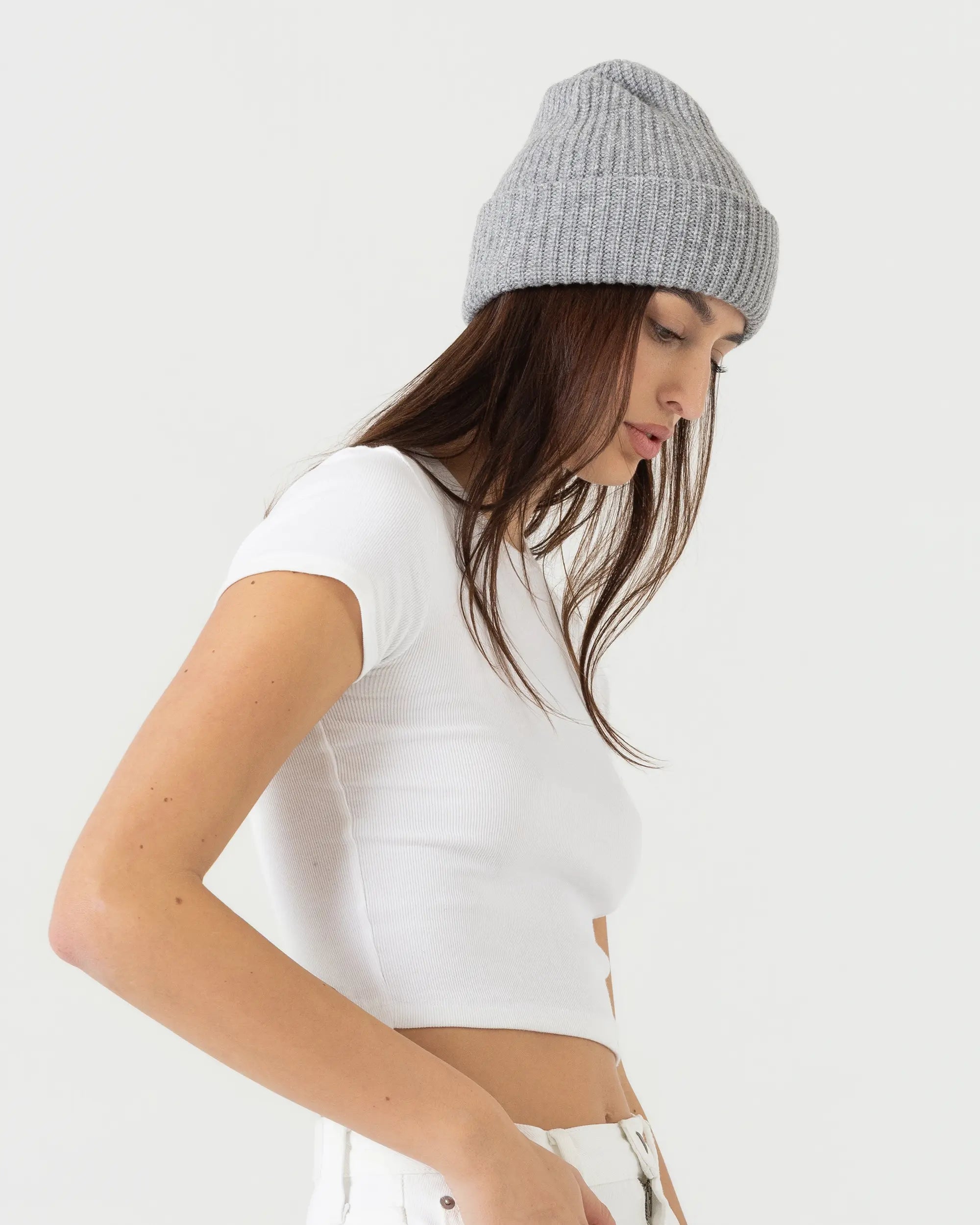 Woman wearing a white crop top and gray beanie on a plain background