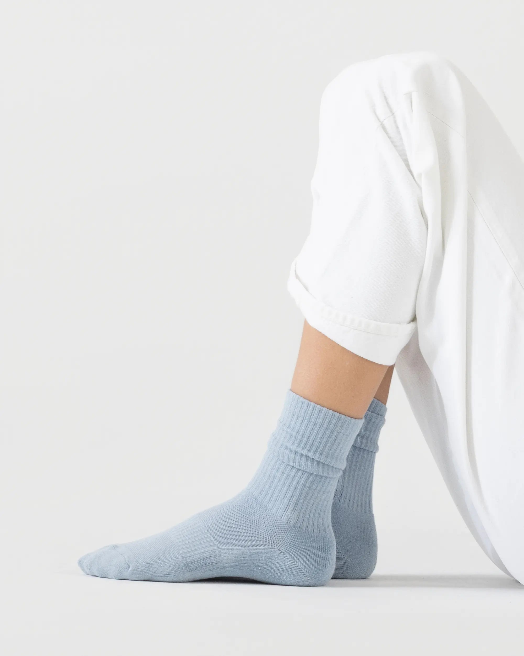 Person wearing light blue sporty socks with a white outfit on a plain background